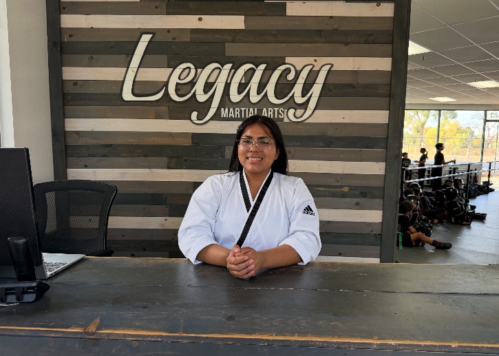 Ms. Rocio Rosales, Enrollment Director, at the front desk beneath the Legacy Martial Arts sign in Oxnard